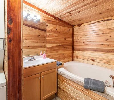 A cozy bathroom with wood-paneled walls and ceiling, featuring a white bathtub, a vanity with a sink, a stacked washer and dryer, and towels neatly placed near the tub.